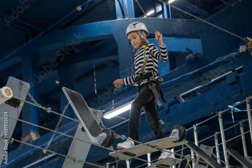 Teenage girl in white helmet calmly overcomes balancing obstacles in rope park