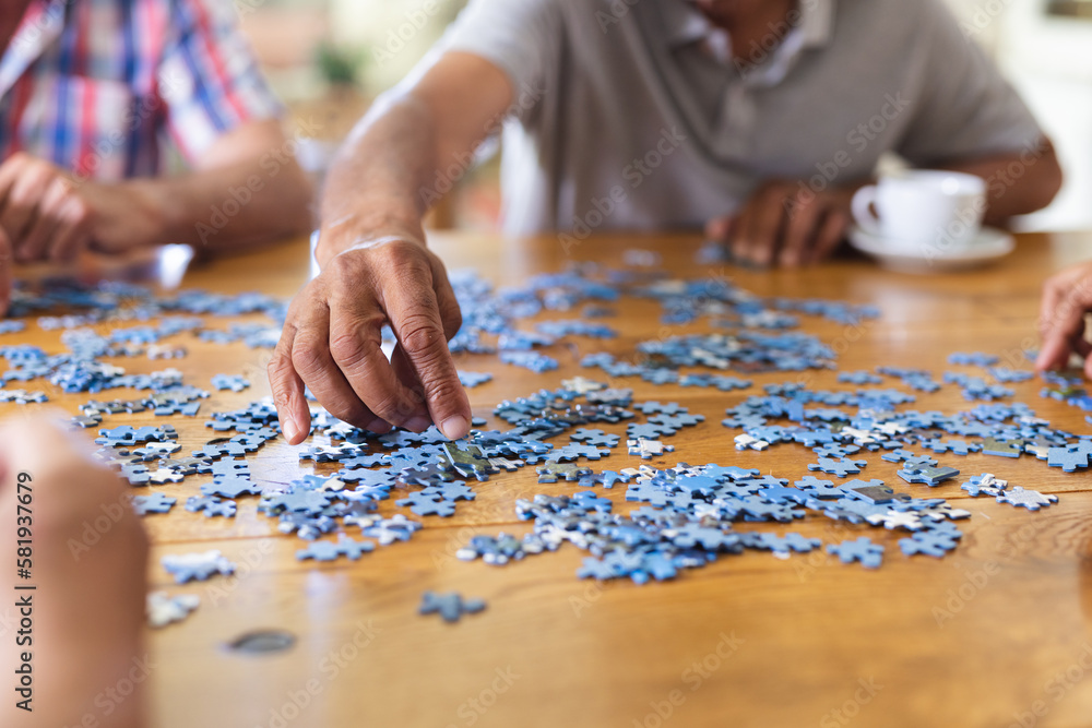 Hands of diverse senior friends sitting at table doing jigsaw puzzle together Hands of diverse senior friends sitting at table doing jigsaw puzzle together