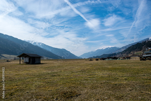 Valley with meadow surrounded by mountains with snowy peaks and blue sky with lots of cloud in Austrian Alps.