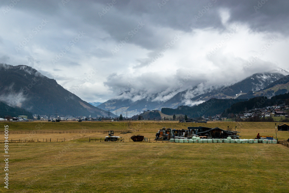 Valley with mountains in clouds in rainy weather in Austrian Alps. Meadow with outbuildings and hay bales.