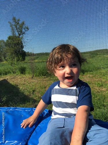 cheerful laughing curly playful little funny boy with beautiful smiling eyes sits on a trampoline