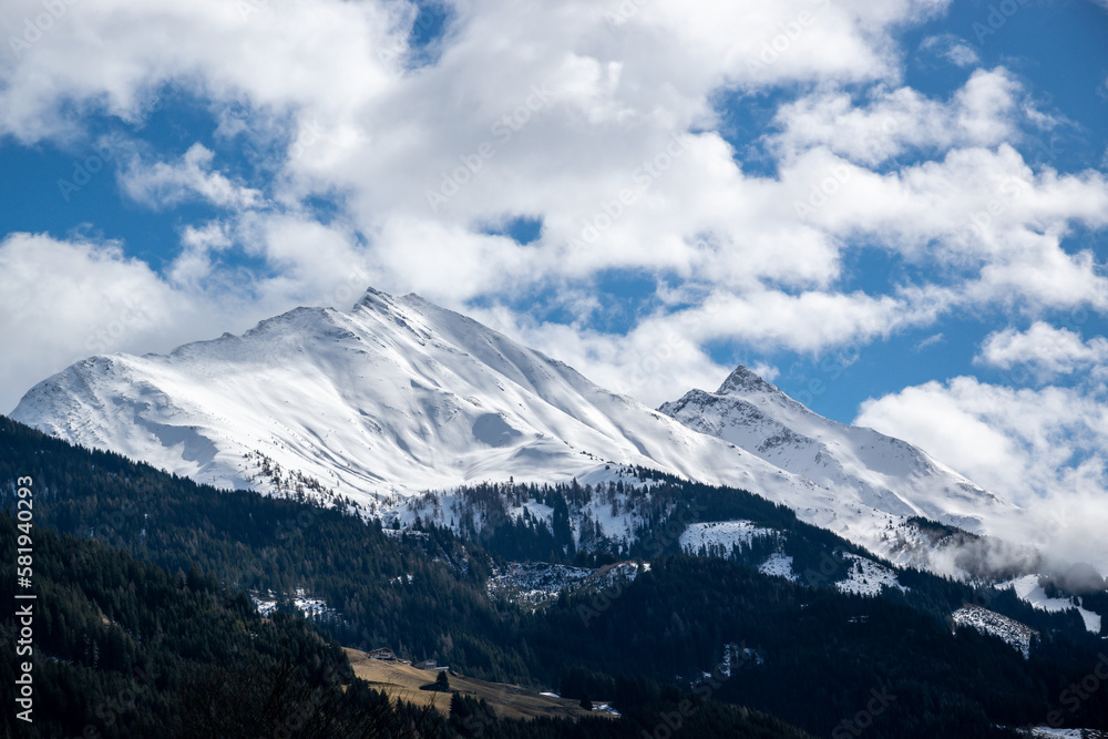 Mountain range of Austrian Alps, pointed rocks covered with snow above forest and meadow in winter.