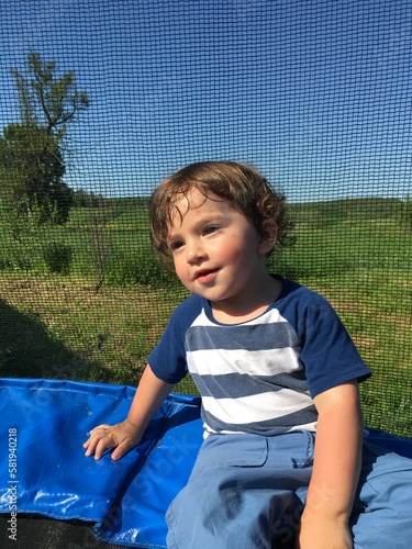 smiling cheerful laughing curly playful little funny child with beautiful eyes sits on a trampoline