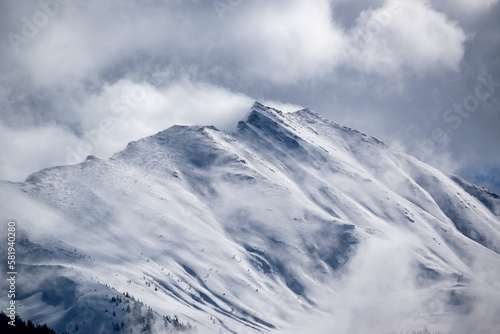 Winter snowy ridge of rocky mountains in the Austrian Alps. Clouds around the top of the hill.