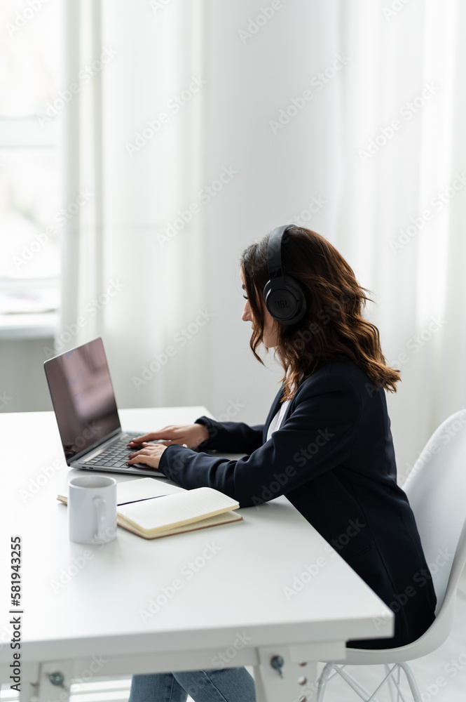 An attractive girl is sitting at a desk near a laptop in headphones An attractive girl is sitting at a desk near a laptop in headphones