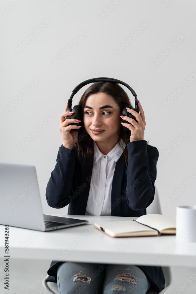 An attractive girl is sitting at a desk near a laptop in headphones An attractive girl is sitting at a desk near a laptop in headphones
