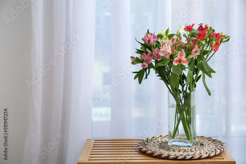 Glass vase with beautiful alstroemeria flowers on wooden table near window