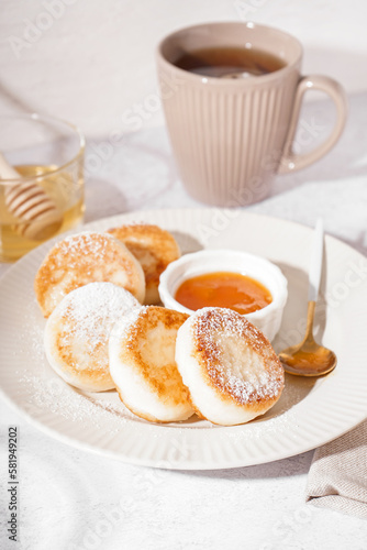 Plate with delicious cottage cheese pancakes, jam and cup of tea on light background, closeup