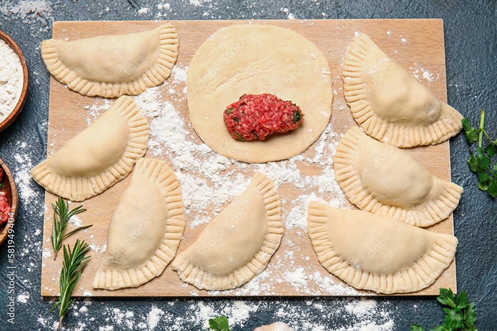 Wooden board with raw meat empanadas on dark background, closeup Wooden board with raw meat empanadas on dark background, closeup
