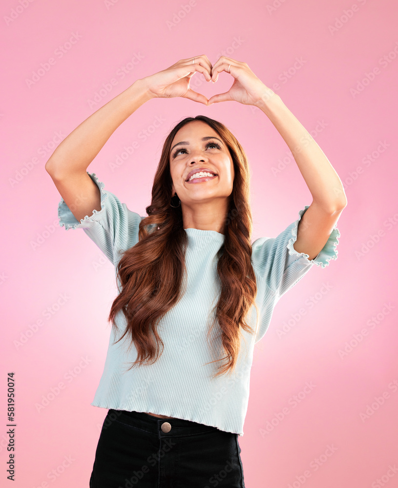 Naklejka premium Happy, heart hands and shape with woman in studio for romance, positive and kindness. Love, support and emoji with female and smile isolated on pink background for emotion, hope and gesture
