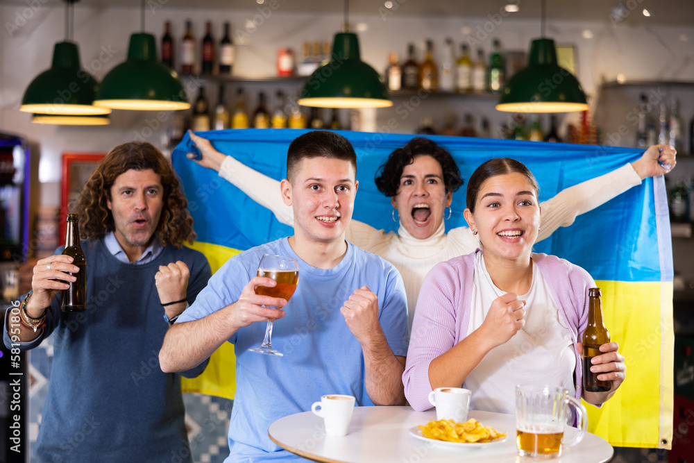 Obraz premium Happy friends of different ages drinking beer and celebrating the victory of the Ukrainian team in the night bar