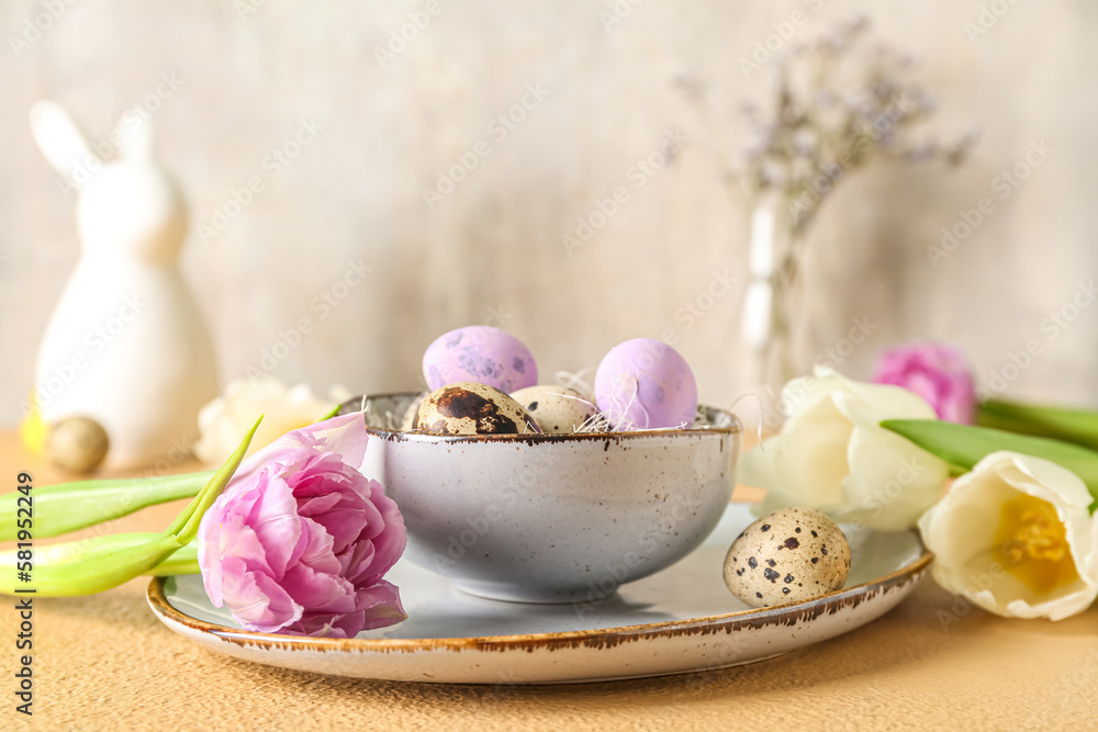 Bowl with Easter quail eggs and tulip flowers on beige table