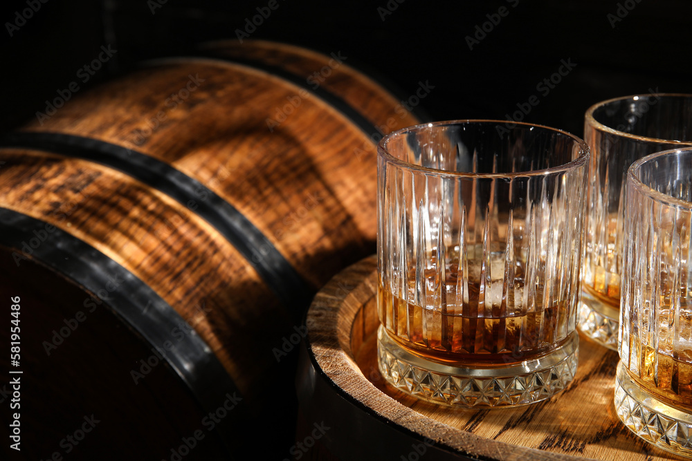 Oak barrels with glasses of cold whiskey on dark wooden background - obrazy, fototapety, plakaty 