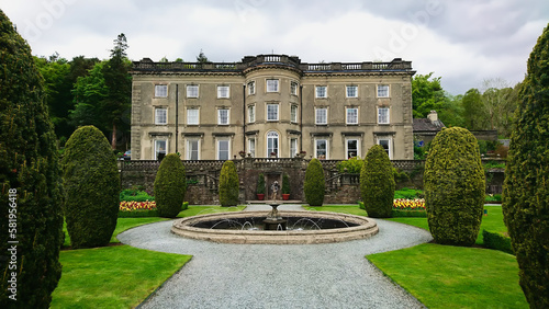 Rydal Mount and Gardens, Lake District, United Kingdom - May 11, 2018: front view of the exterior of the facade of the garden and house with a fountain in the front under a cloudy sky