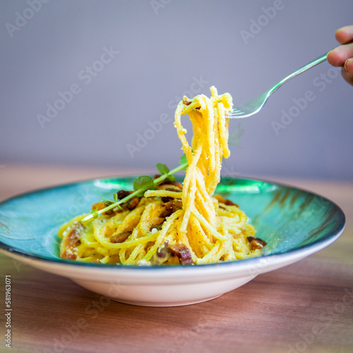 A bowl of pasta with a fork is being held by a person.