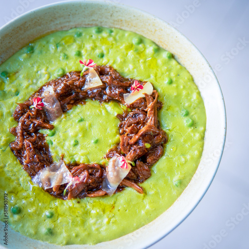 A bowl of green soup with a brown sauce and a red and white sticker on the bottom.