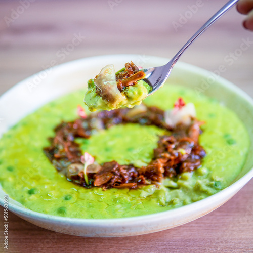 A bowl of green soup with a brown sauce and a red and white sticker on the bottom.