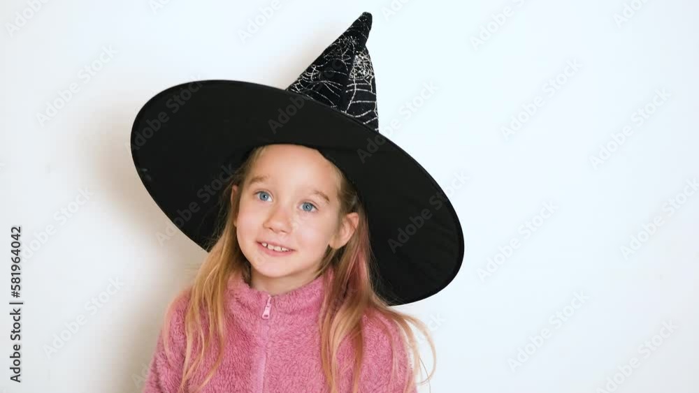 A little blond girl in black witch hat is actively telling something and looking at the camera. The girl sings or recites a poem. Video portrait. 4k resolution video. A little blond girl in black witch hat is actively telling something and looking at the camera. The girl sings or recites a poem. Video portrait. 4k resolution video.