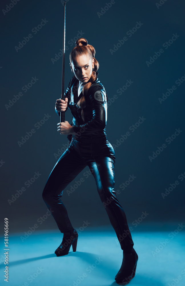 Woman, warrior and vigilante in cosplay with sword stance for battle, war or game against dark studio background. Female in black widow costume standing ready with blade for halloween or hunger games