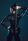 Woman, warrior and back of vigilante with sword in cosplay for battle, war or game against a dark studio background. Rear view of female in black costume with blade for halloween or hunger games