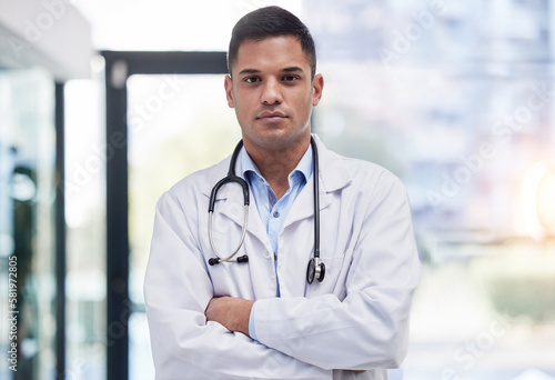 Portrait, man and doctor with arms crossed, focused and confident in hospital, clinic and surgery. Serious, proud and young medical worker in lab coat for healthcare services, wellness and commitment