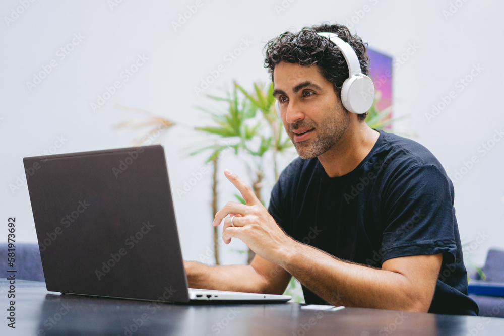 Middle-aged Latin teacher wearing headphones giving a class from his living room via the Internet. Middle-aged Latin teacher wearing headphones giving a class from his living room via the Internet.