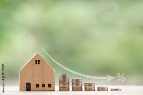 Model wooden house in front of a natural green backdrop and an arrow showing a falling rate of interest. Strategic ideas to get lower interest rates when buying and mortgage a home.