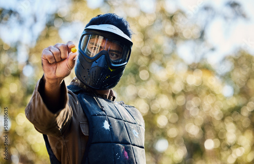 Man, paintball and hands holding ball on the battlefield for war, shot or engaging act in nature. Male paintballer or soldier showing or pinching paint bullet in military or extreme adrenaline sports photo