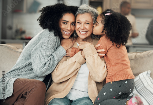 Kiss, portrait and grandmother with girl and woman on a sofa, hug and happy in their home together. Kissing, face and excited senior woman with adult daughter and grandchild on couch, bond and smile