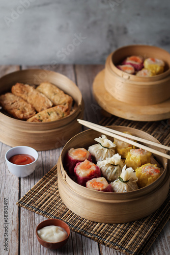 dim sum dumplings in bamboo steamer with sauce on wood table