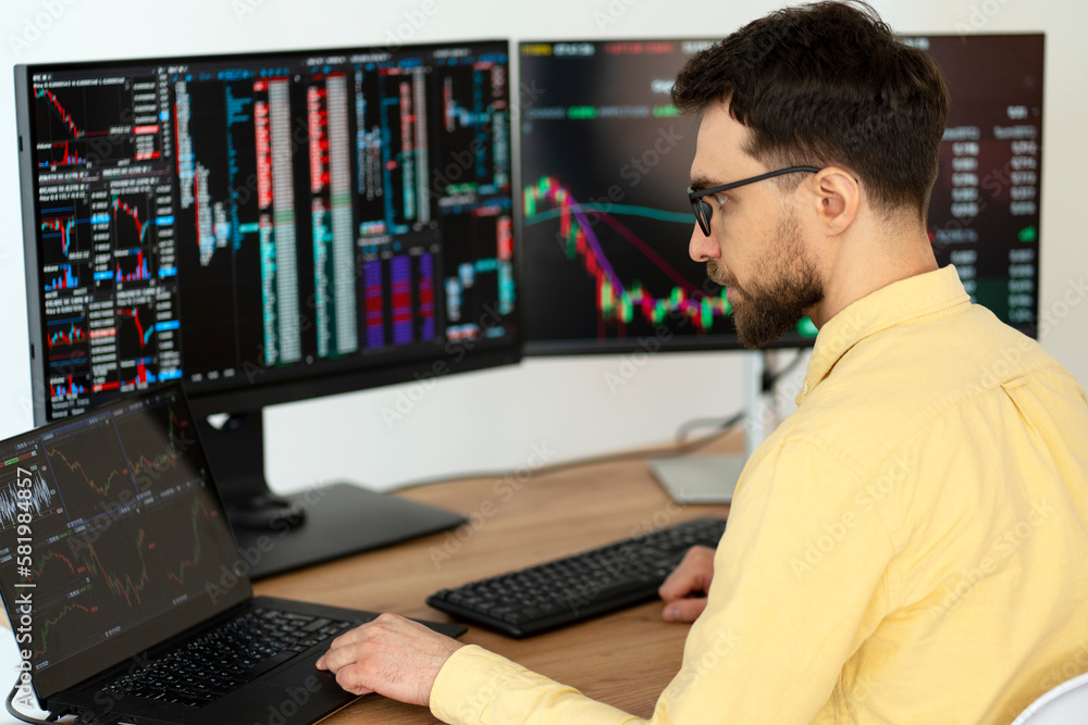 Serious handsome man trader using laptop computer working online with crypto chart sitting in modern office. Broker research stock market. Successful business, online trading concept Serious handsome man trader using laptop computer working online with crypto chart sitting in modern office. Broker research stock market. Successful business, online trading concept