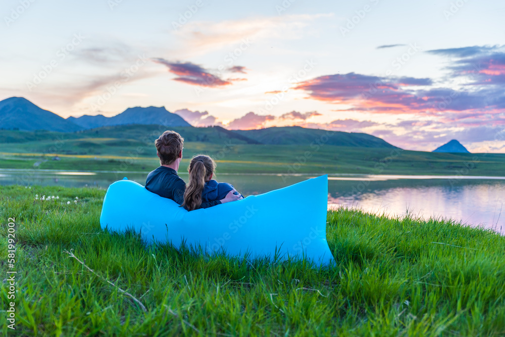 Couple Sits Near Mountain Lake at Sunset