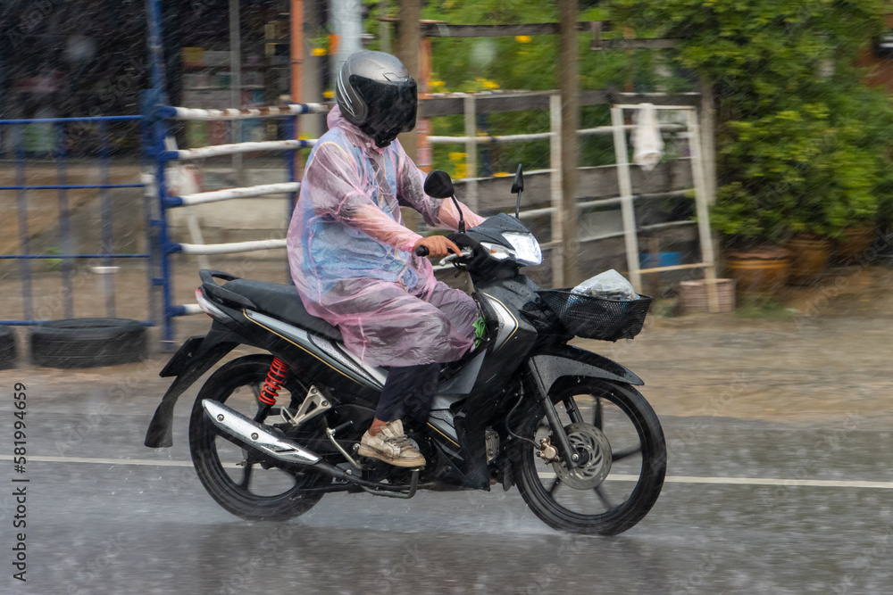 A man in a raincoat rides a motorcycle on the street in heavy rain, Thailand