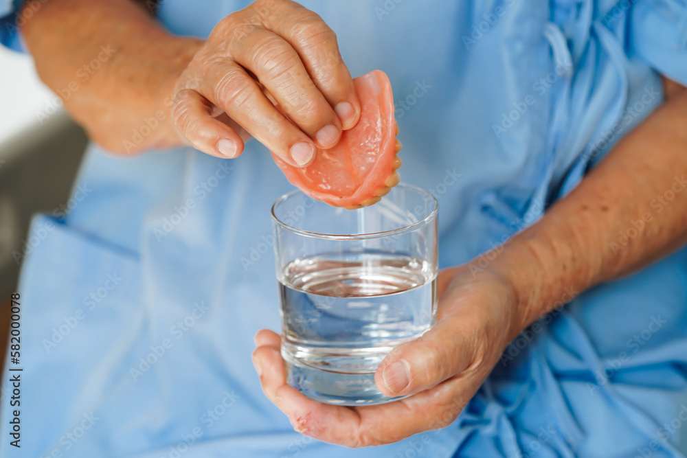 Asian senior woman patient clean teeth denture in a glass with solution for chew food. Asian senior woman patient clean teeth denture in a glass with solution for chew food.