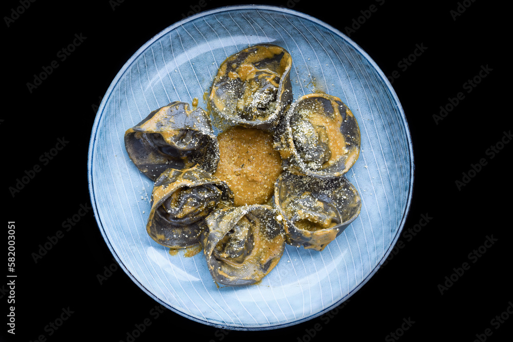 Ravioli with chicken and mushrooms inside and grated cheese on blue plate isolated on black background Ravioli with chicken and mushrooms inside and grated cheese on blue plate isolated on black background