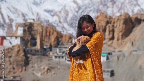 Portrait of beautiful Indian teenager girl playing with cute puppy while standing against Dhankar Monastery and snow clad mountains in Spiti Valley, India. Concept of love and care for pets  photo