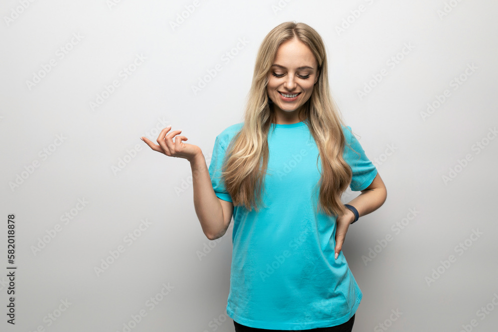 Fototapeta premium blond young woman in a blue t-shirt points to an empty space on a white background