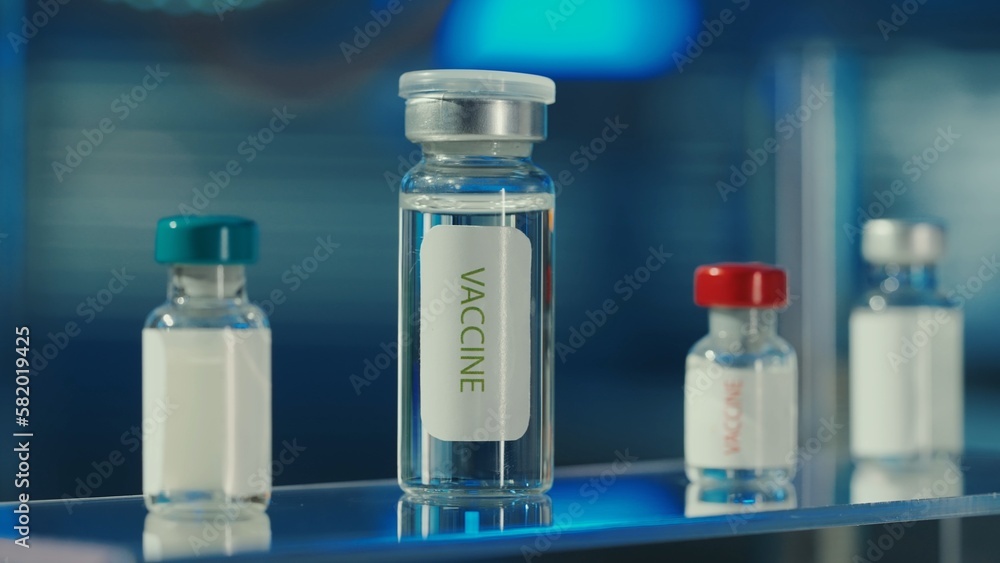 Glass vials with a vaccine on a blurred laboratory background. Bottles with clear liquid and light reflection. Medical background, close up.