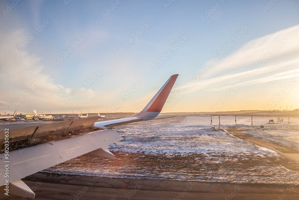 The plane is dressed for takeoff. Aircraft's wing and land seen through the illuminator. View from the window of the plane. Airplane, Aircraft. Traveling by air. Airplane flight at sunset or dawn. 