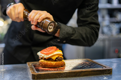 chef hand cooking cheeseburger with vegetables and egg on restaurant kitchen