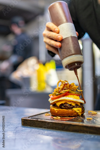 chef hand cooking cheeseburger with vegetables and egg on restaurant kitchen