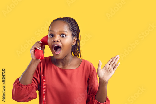 Canvas Print Portrait of stunned African American woman isolated on yellow studio background talk on corded phone