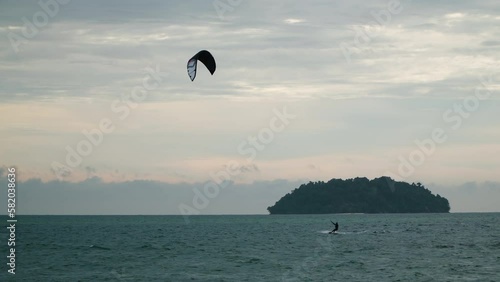 Man kitesurfer  jumps high while kitesurfing at sunset near island in Malaysia - wide angle tracking shot