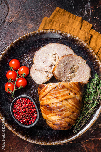 Baked delicious beef meatloaf, sliced meat loaf with bacon and herbs on a plate. Dark background. Top view photo