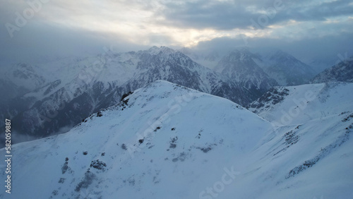 Mystical dawn with clouds in snowy mountains. The white hills are covered with clouds and snow. Steep rocky cliffs. The high peaks of the peaks. The rays of the sun at dawn pass through the clouds