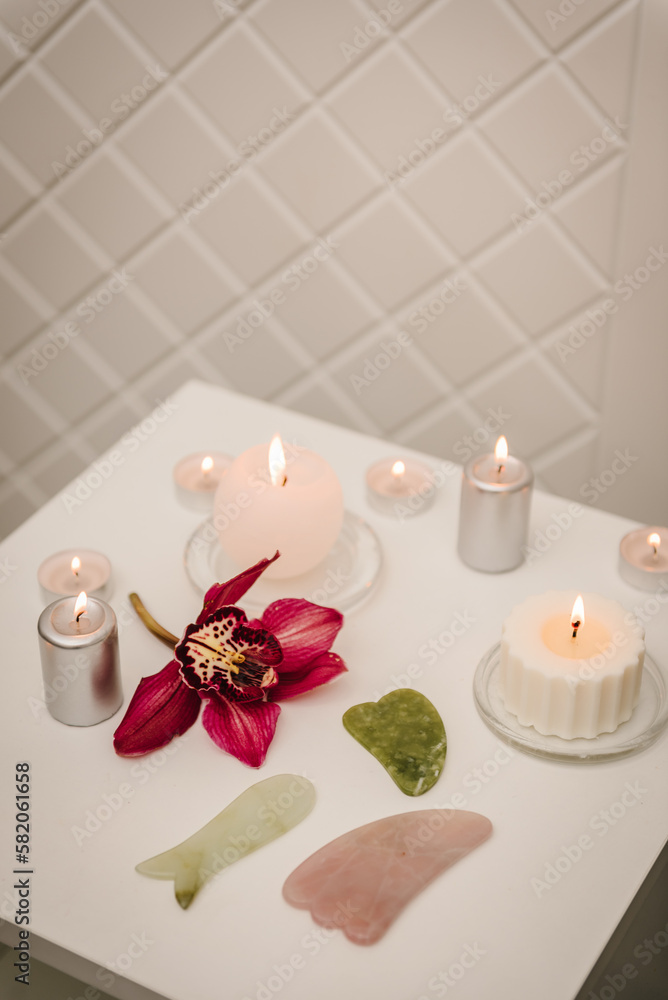 Gua sha tool. Candles, and orchid flowers on table. Facial massage for lifting, face therapy, home spa, mockup. Skincare concept. Cosmetology, body massage, spa procedure. Details decor in spa salon.