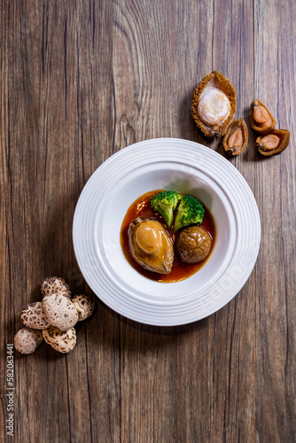 Obraz na płótnie expensive premium braised head abalone with sea cucumber and flower mushroom broccoli in thick golden sauce on wood table asian chinese halal deluxe banquet seafood menu w salonie