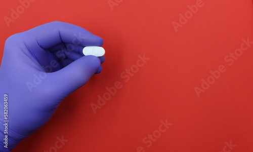 Hand of doctor or researcher showing a drug, ibuprofen, or antibiotic pill on a red background