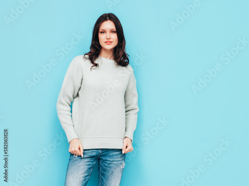 Young beautiful smiling female in trendy summer jeans and warm winter sweater clothes. Sexy carefree woman posing near blue wall in studio. Positive model. Cheerful and happy. Isolated.