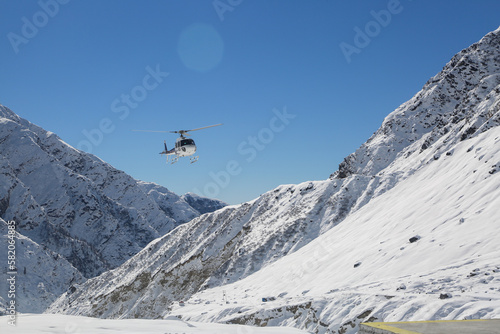 Helicopter flying in snow covered valley of Mountain in Himalaya. White helicopter on a white landscape with clear blue sky background. 